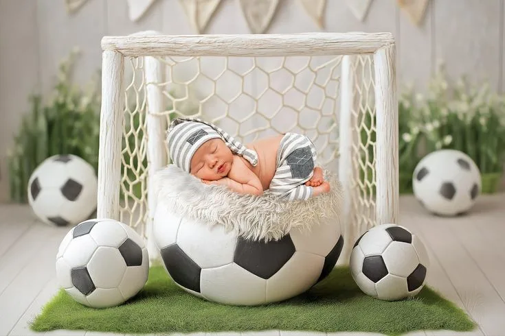 Sleeping newborn in a football-shaped bowl in front of a miniature goal