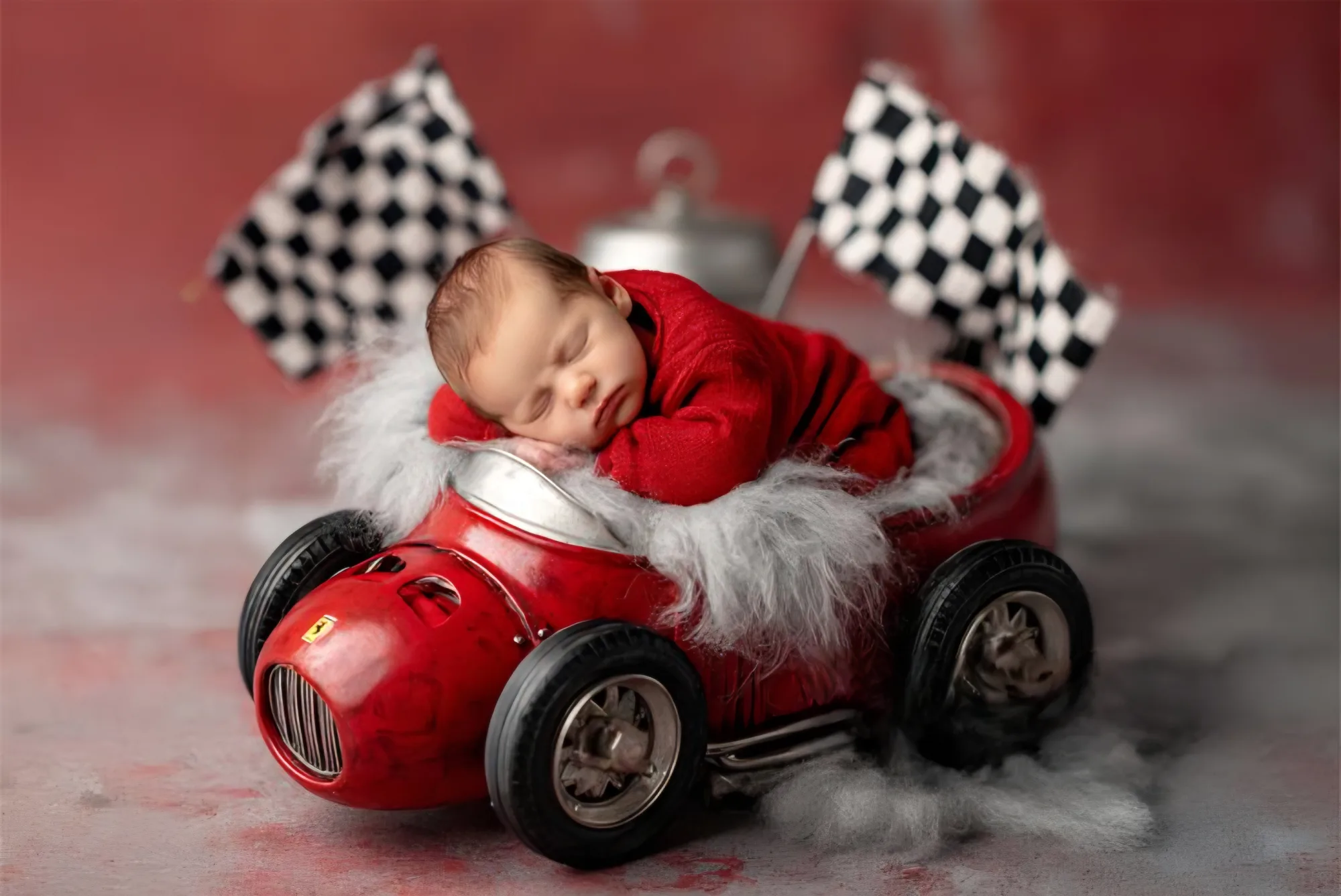 Sleeping baby in a red racing car with chequered flags
