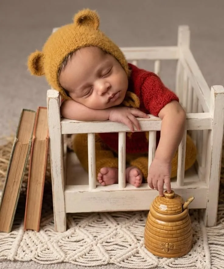 Sleeping baby in a teddy-style hat on a wooden chair beside a honey pot
