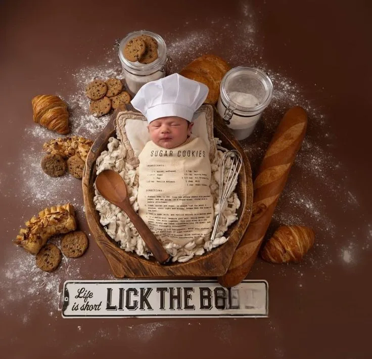 Sleeping baby in a baker outfit among croissants, cookies and baking ingredients