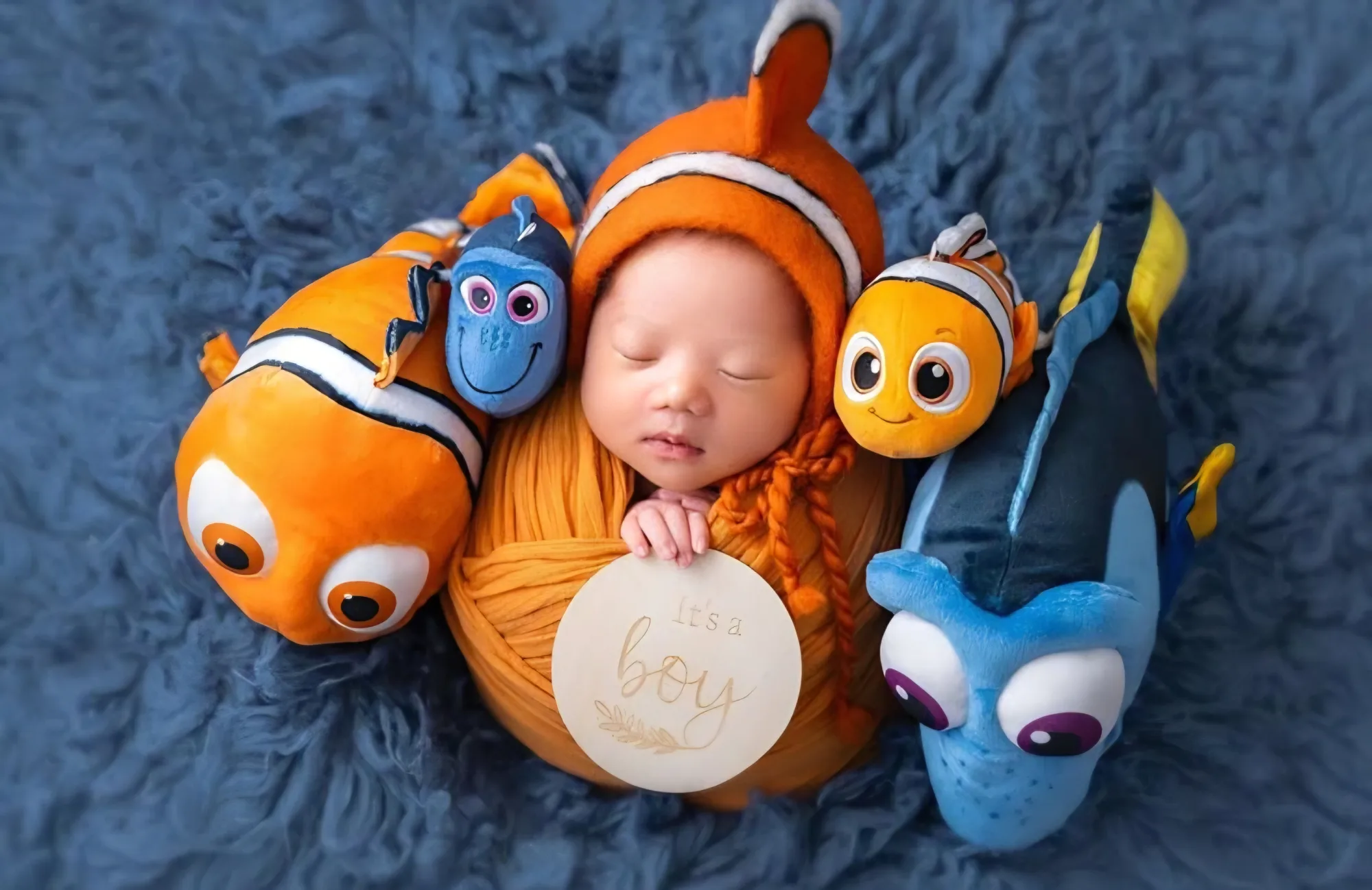 Baby in an orange outfit surrounded by plush ocean fish