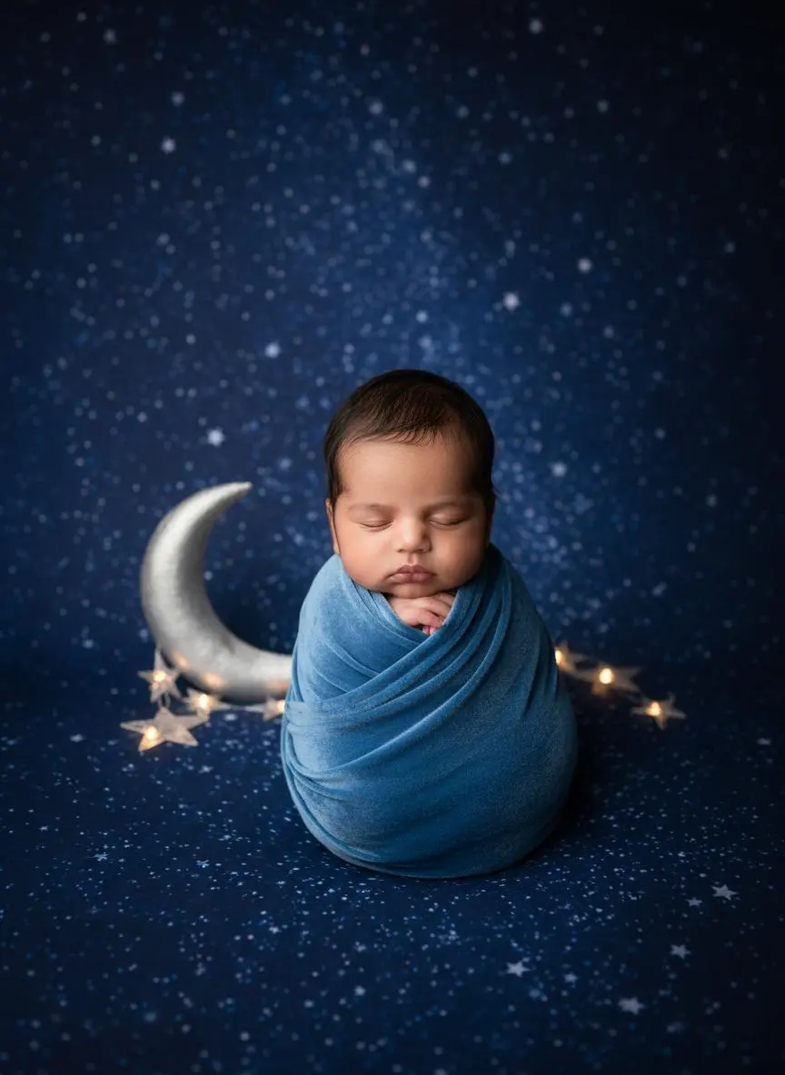 Swaddled baby in blue under a starry sky with a crescent moon